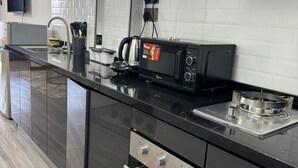 Eine moderne Küche mit schwarzem Arbeitsplatz, einer Mikrowelle, einer Kaffeemaschine und einer Edelstahl-Dunstabzugshaube.