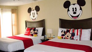 Deux lits d’hôtel avec des têtes de lit décorées aux couleurs de Mickey Mouse, des couvre-lits rouges et des oreillers.