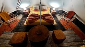 Habitación tipo tienda de campaña con una cama central, dos mesitas auxiliares, sillas de mimbre y una mesa de madera en el centro.
