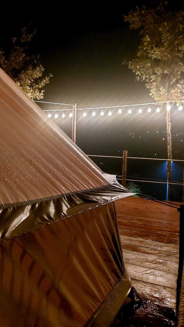 A tent with a waterproof covering, a wooden deck, and string lights in the background. - Welcome Love - Eco Camping Resort (Cinfães)