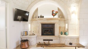 A cozy room with a fireplace, a television mounted on the wall, and a rustic wooden table with various items. - Country Trullo Rosso With Jacuzzi Alberobello (Alberobello)