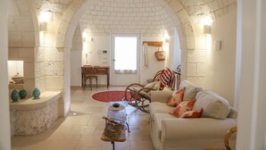 A cozy living room with a stone archway, a sofa, a coffee table, and a dining area with a chair and table. - Country Trullo Rosso With Jacuzzi Alberobello (Alberobello)