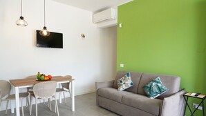 Un saló amb un sofà gris, una taula de dinar de fusta amb cadires, un televisor de pantalla plana i una paret d'accent verd.