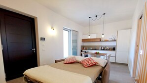 A bedroom with a bed, a desk, and a kitchenette.