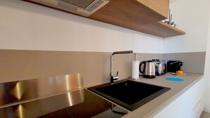 A modern kitchen with a stainless steel sink, a coffee maker, and a kettle on the countertop.