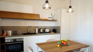 A modern kitchen with a wooden table, white chairs, and a variety of appliances including a stove, oven, and coffee maker.