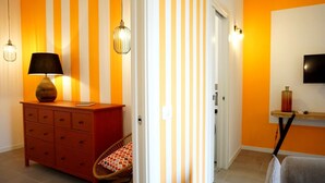 A room with a wooden dresser, a chair, a lamp, and a television on the wall.