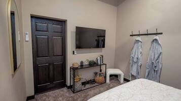 A bedroom with a bed, a TV mounted on the wall, a small table with a basket, and a door.