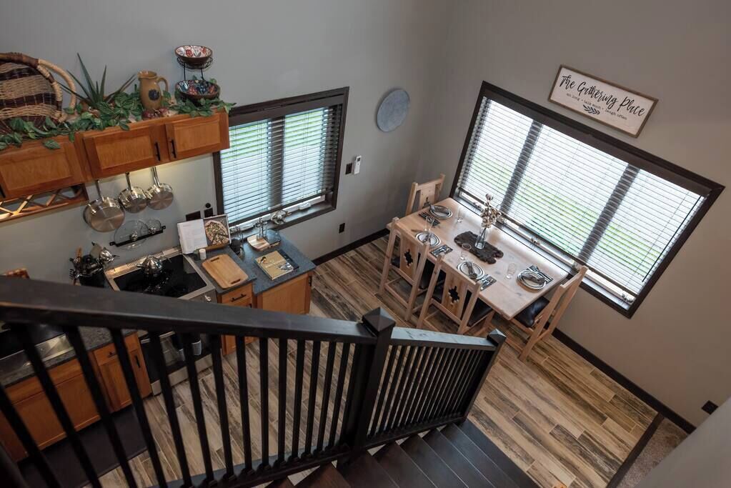 Una cocina con armarios de madera, un comedor con mesa y sillas, y ventanas amplias con persianas.