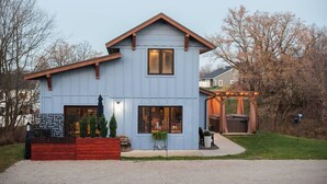 Une maison à deux étages, à la façade bleue, avec un porche à l’avant doté d’un banc en bois et un petit jardin agrémenté de plantes en pot.
