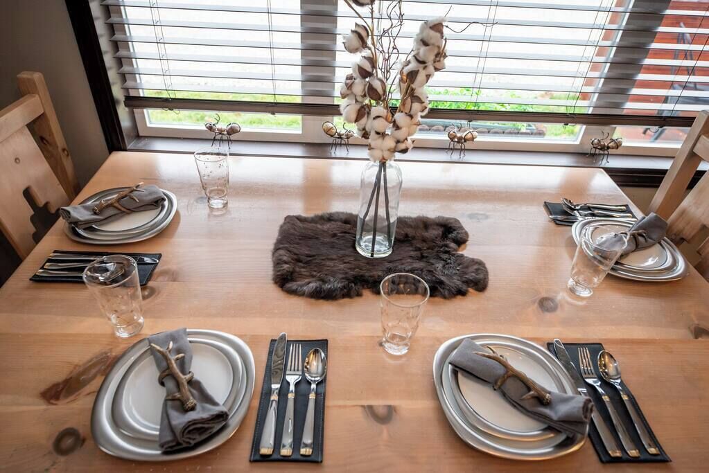 Een eettafel gedekt voor vier personen, met borden, bestek en glazen. Een vaas met gedroogde bloemen staat in het midden op een vachtonderzetter.