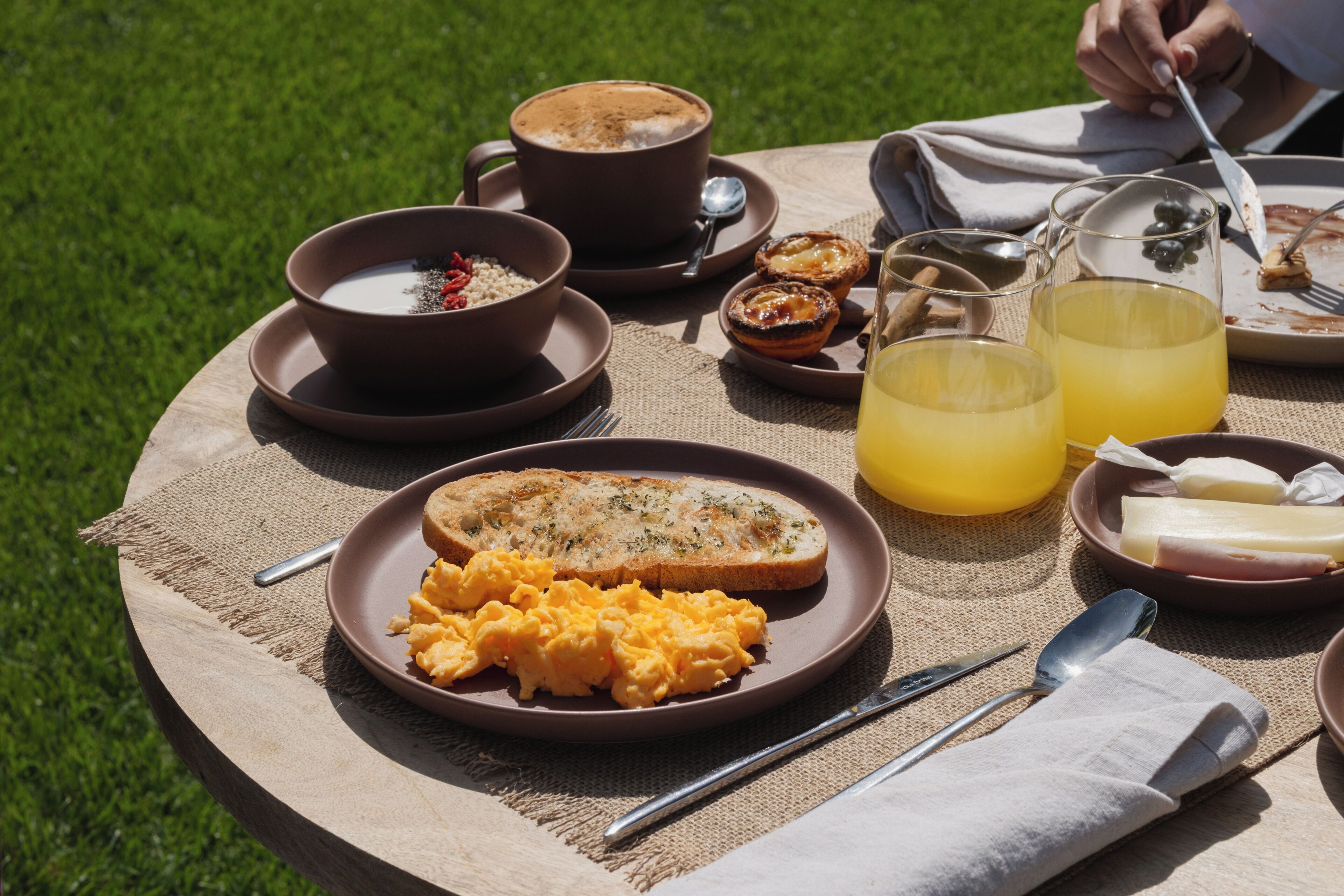 A round wooden table with breakfast items including scrambled eggs, toast, coffee, and juice.