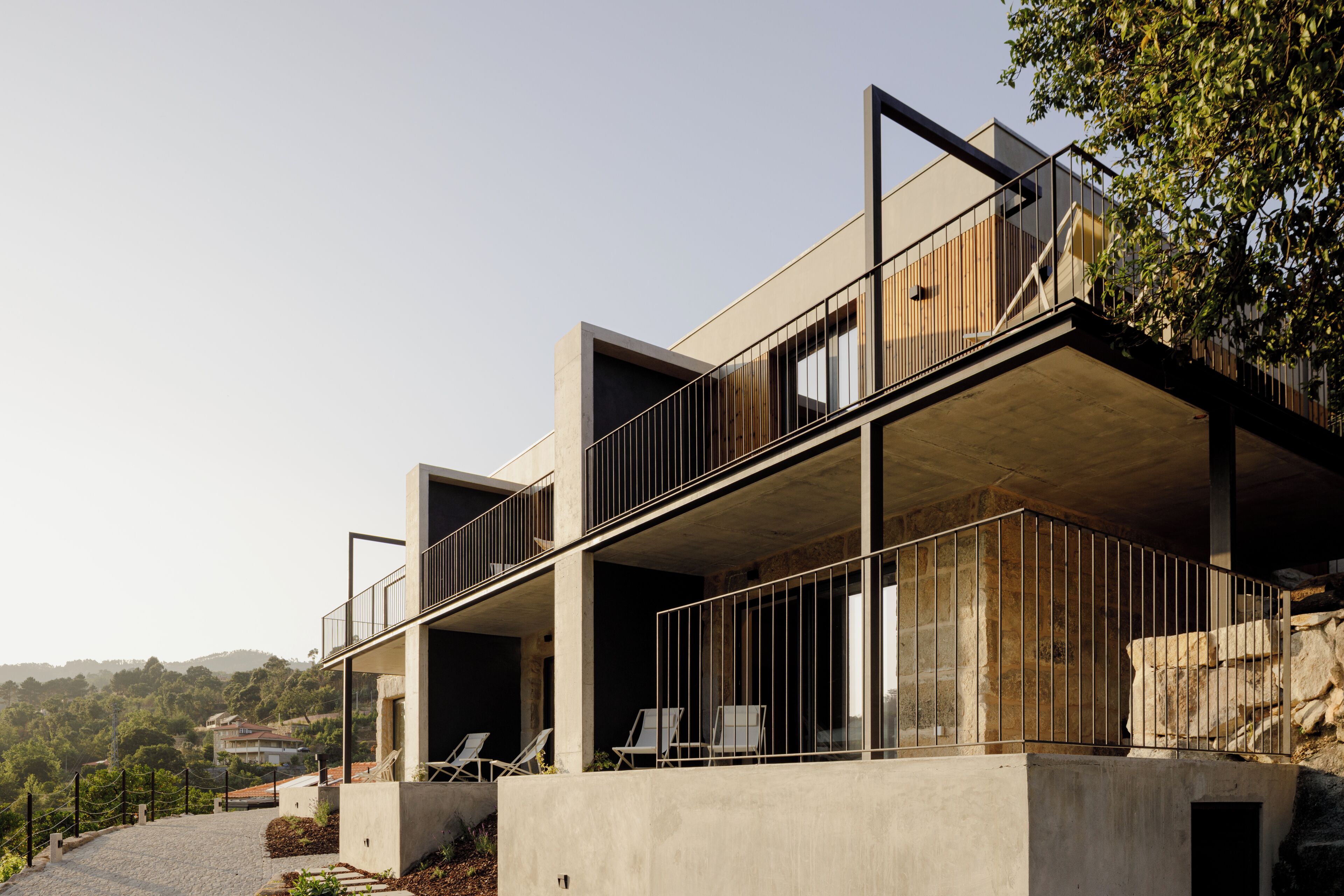 A modern building with a balcony, a stone wall, and a view of the surrounding landscape.