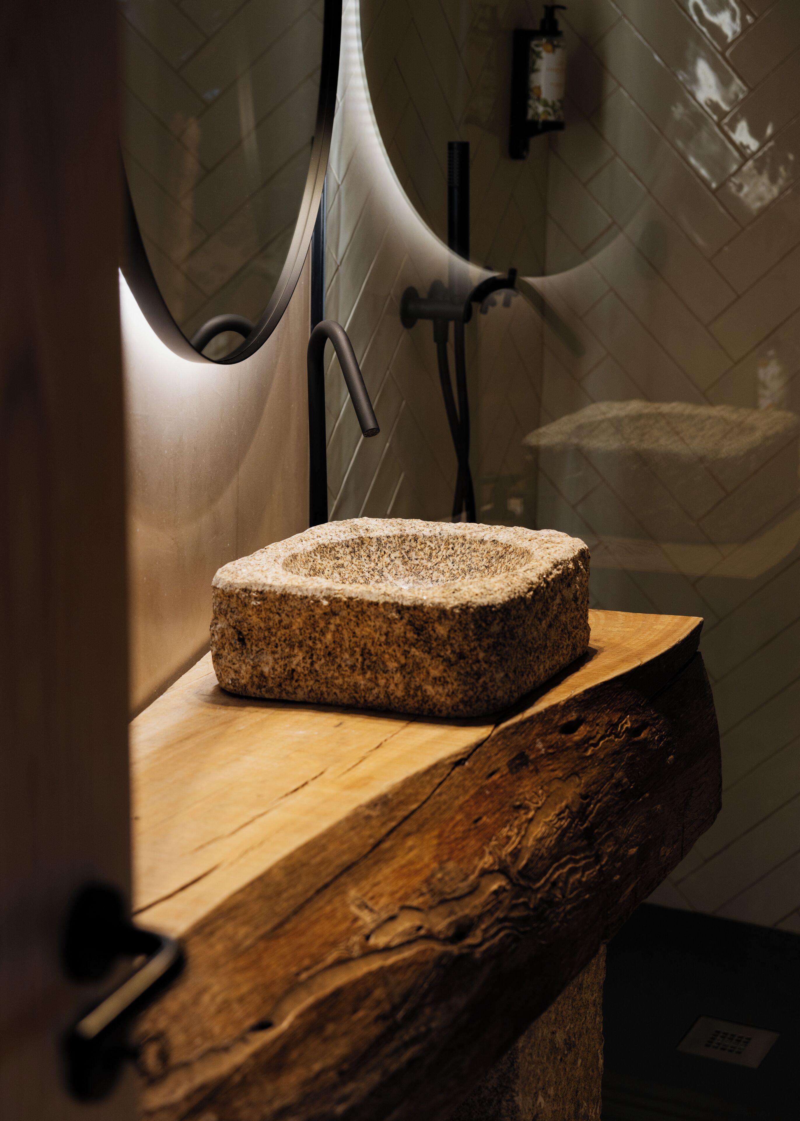 A stone cutting board on a wooden countertop in a bathroom with a tiled wall and a towel rack.