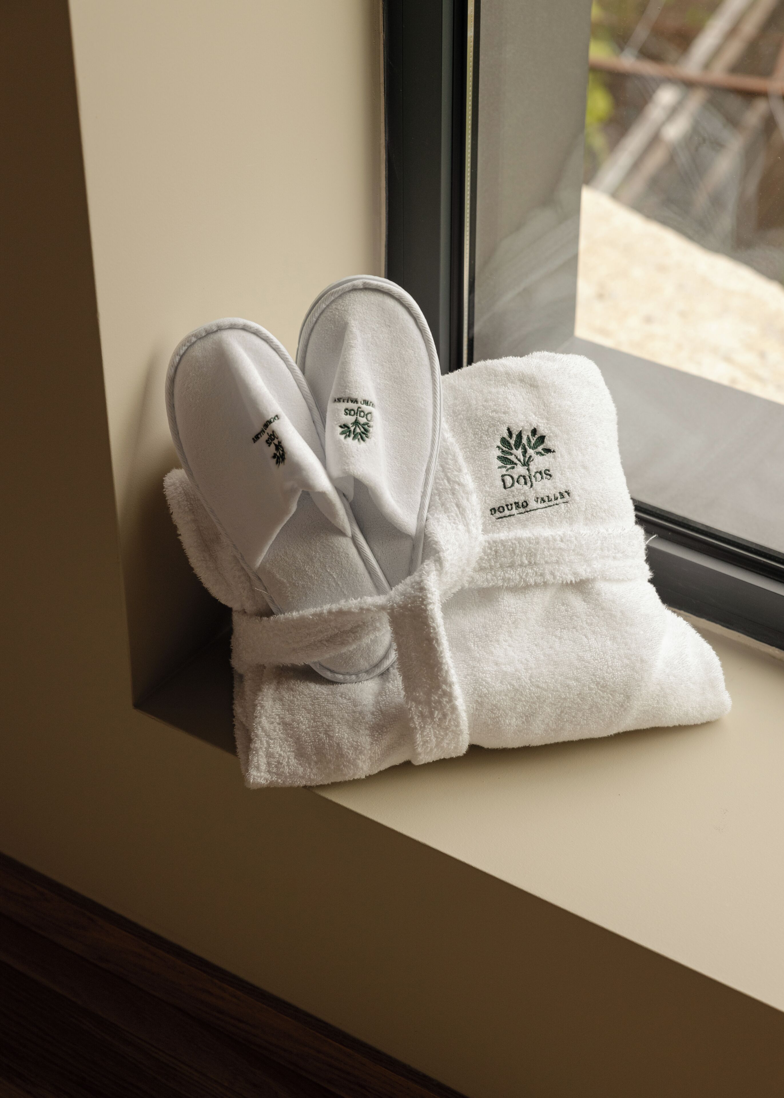 A pair of white slippers with embroidered text and a logo, placed on a window sill.