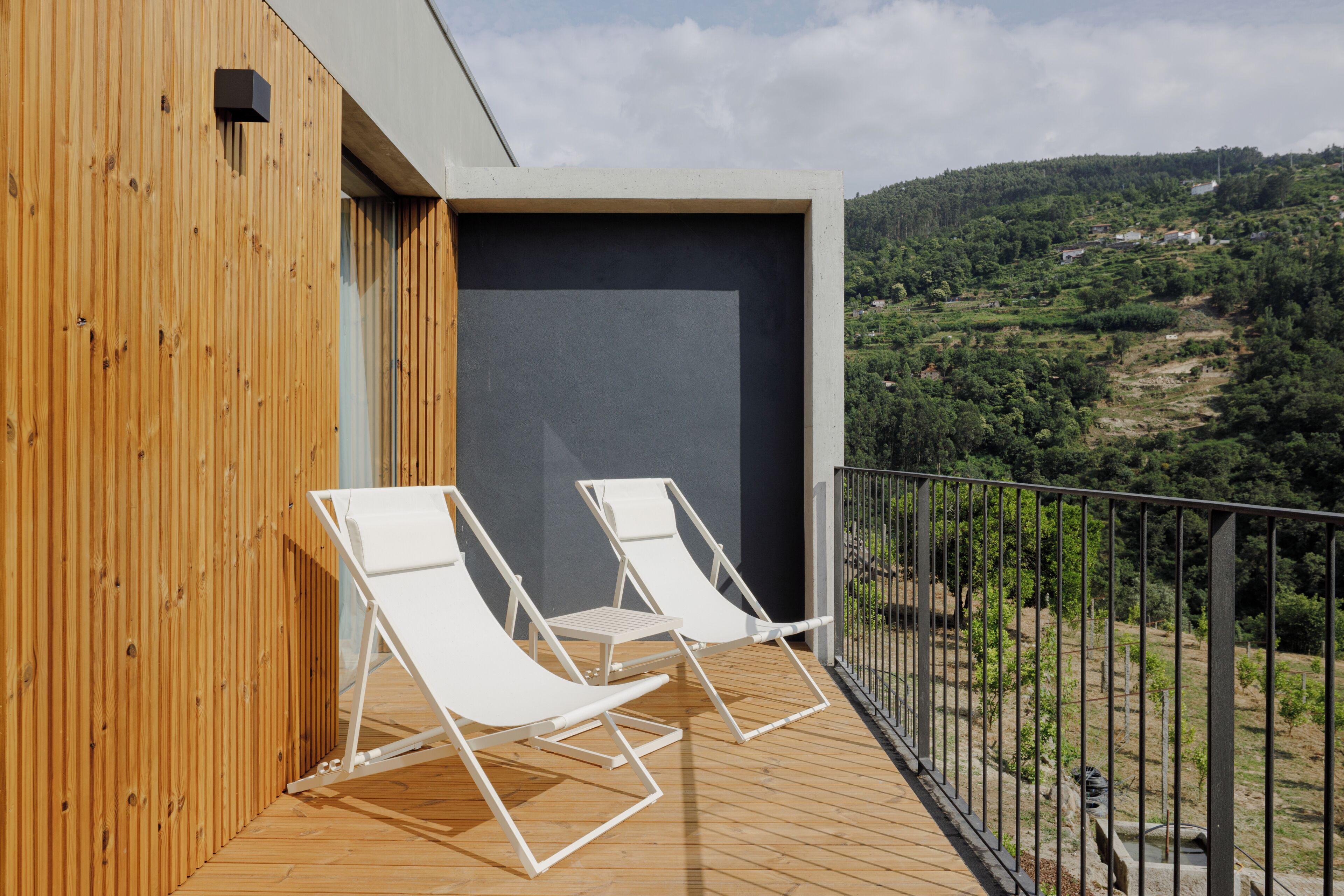 Un balcón con dos sillones blancos, una terraza de madera y vistas a un paisaje montañoso.