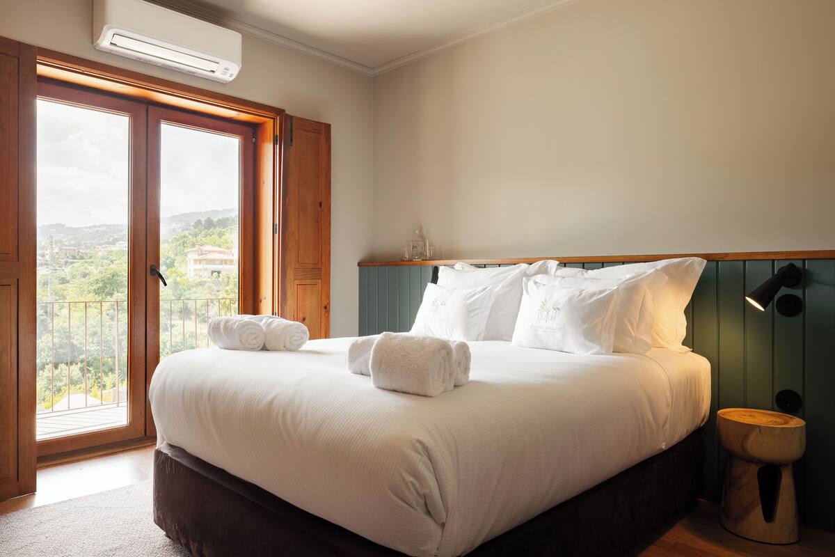 A bedroom with a large bed, a wooden headboard, a bedside table with a lamp, and a view through a glass door.