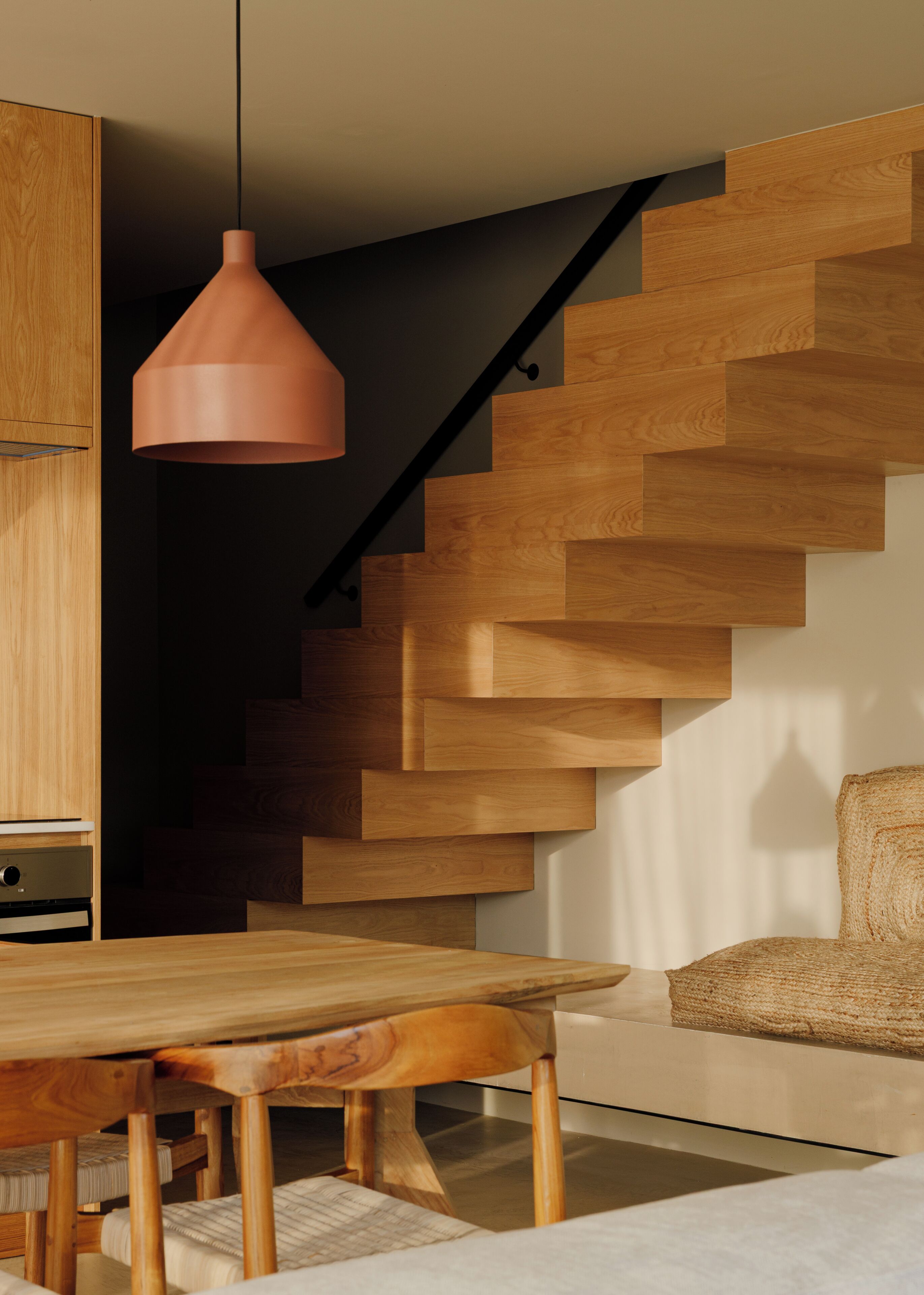 A modern interior with a wooden staircase, a dining area with a table and chairs, and a hanging pendant light.