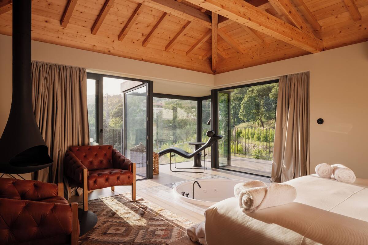 A modern bedroom with a large window, a bathtub, and a cozy seating area.