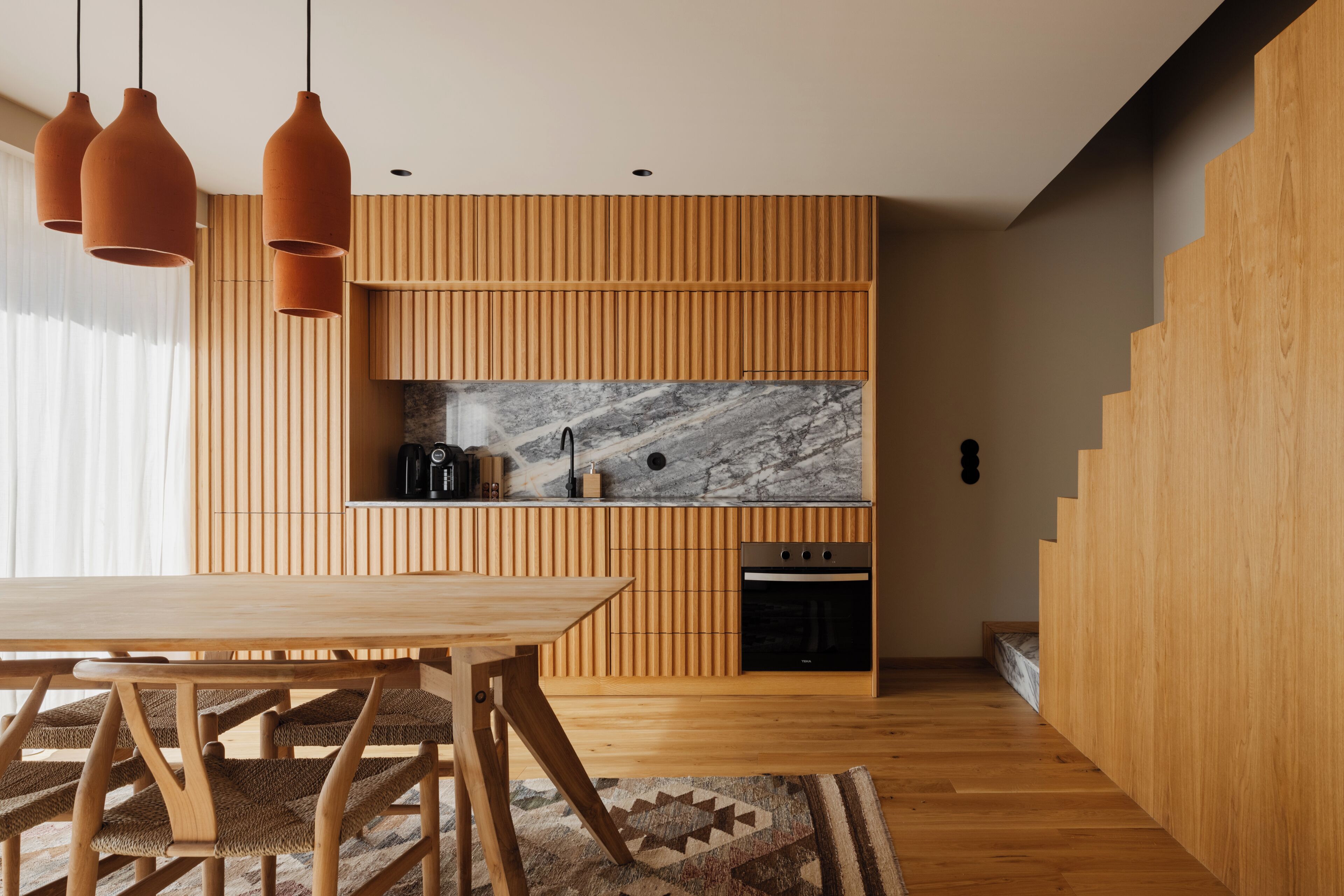 Une cuisine moderne avec un lambris en bois, un pare-feu en marbre et des luminaires suspendus.