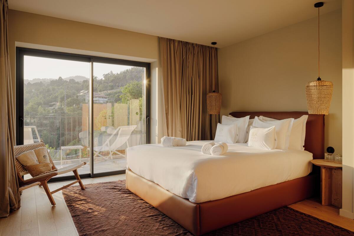 A bedroom with a large bed, a chair, a nightstand, and a view of a balcony.