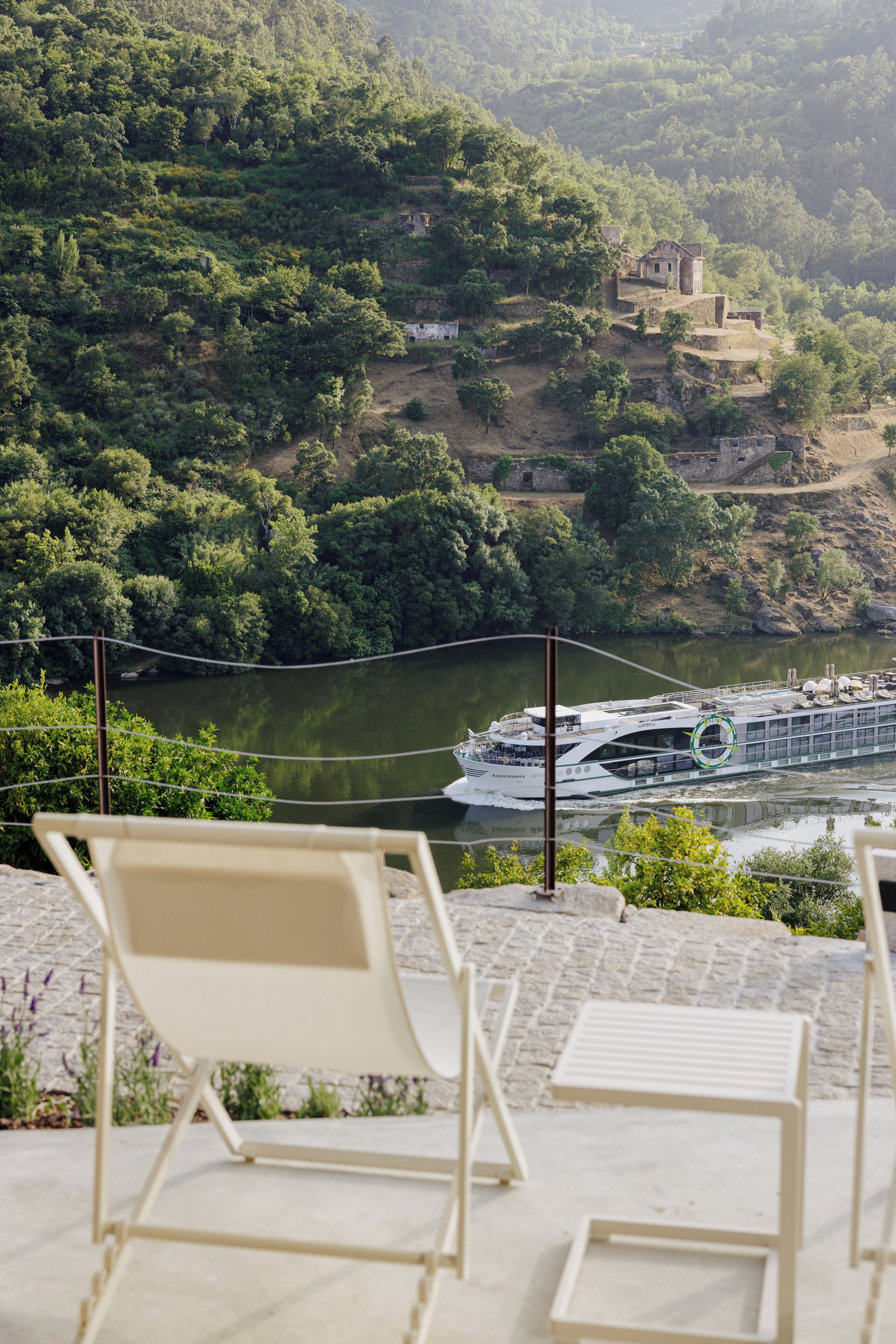 A river with a boat, chairs, and a building on a hillside.