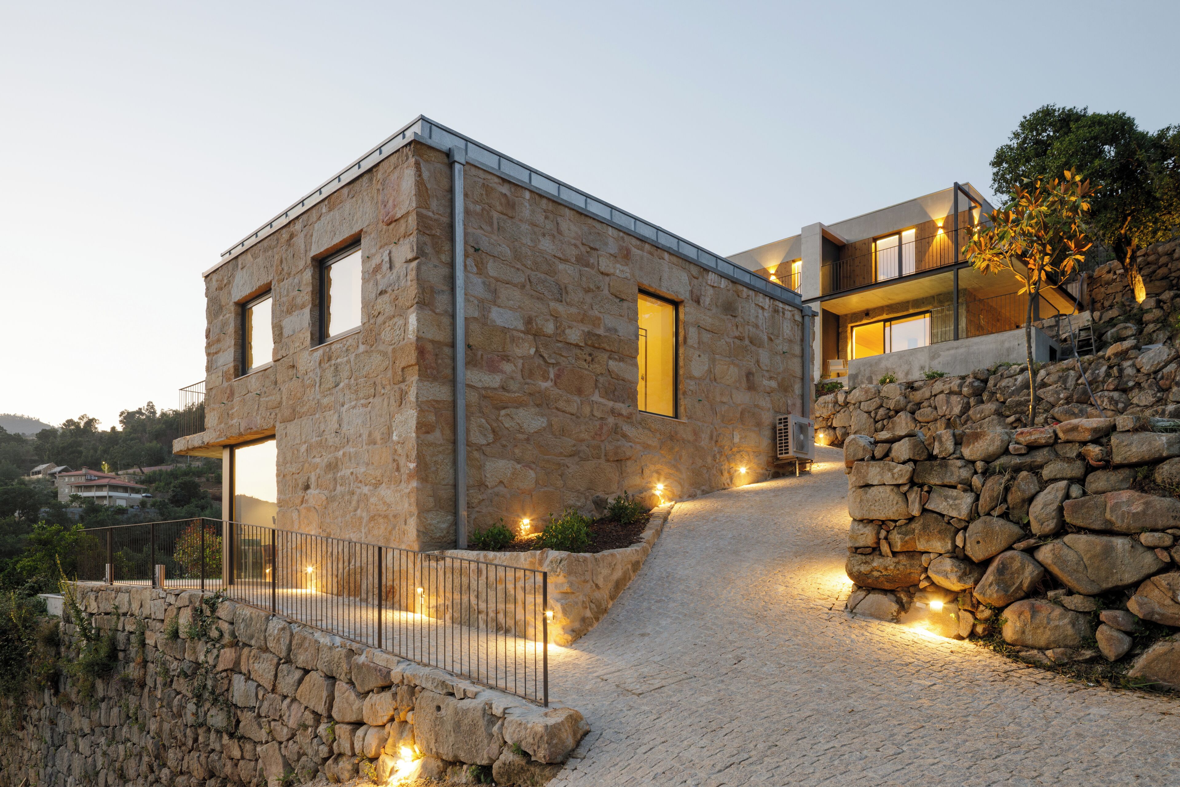 A modern stone building with a balcony, a stone wall, and a paved path.