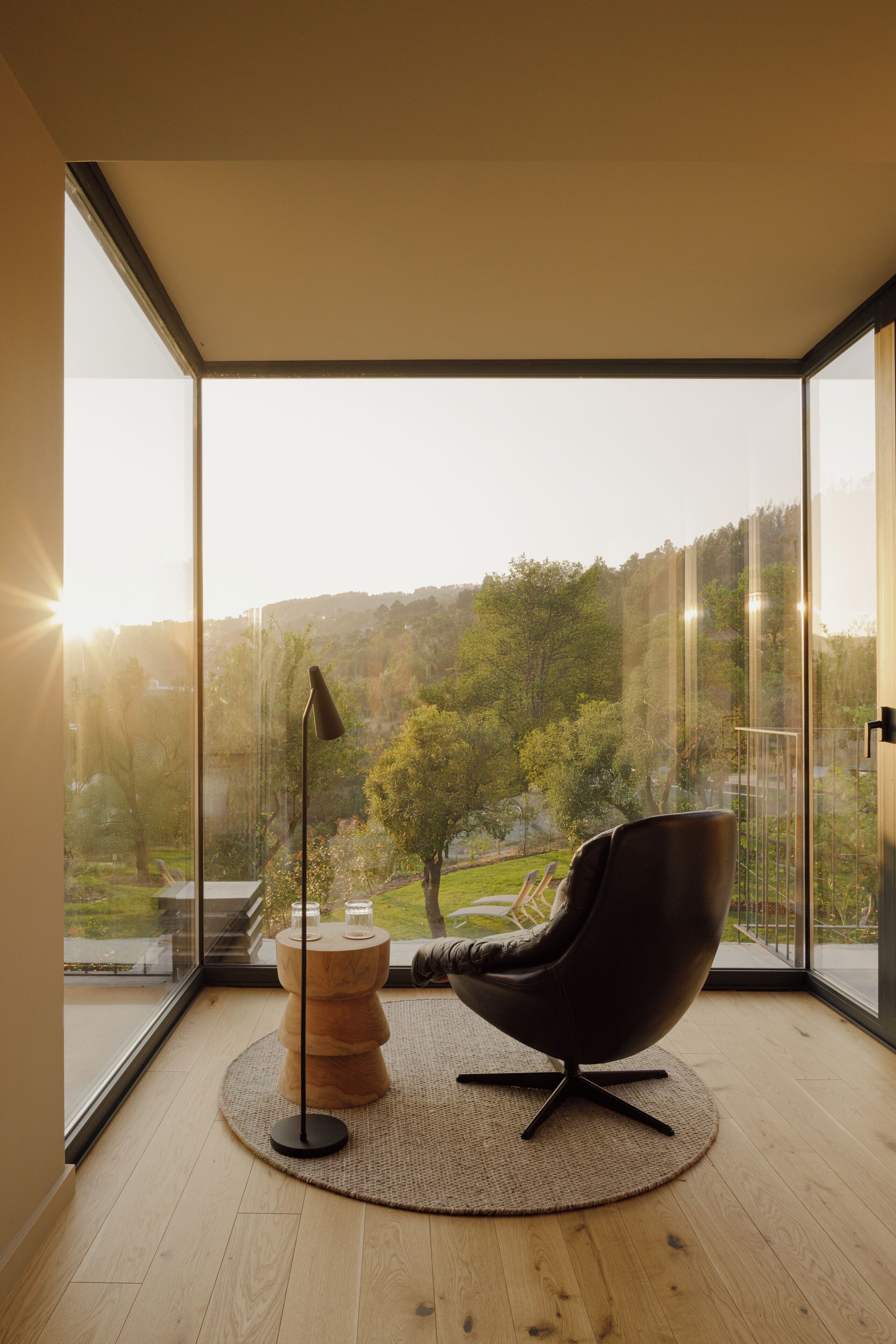 A modern room with a large window, a round wooden table, a black chair, and a floor lamp.