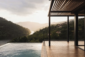 Una terraza de madera con piscina, con vistas a un valle y una masa de agua.