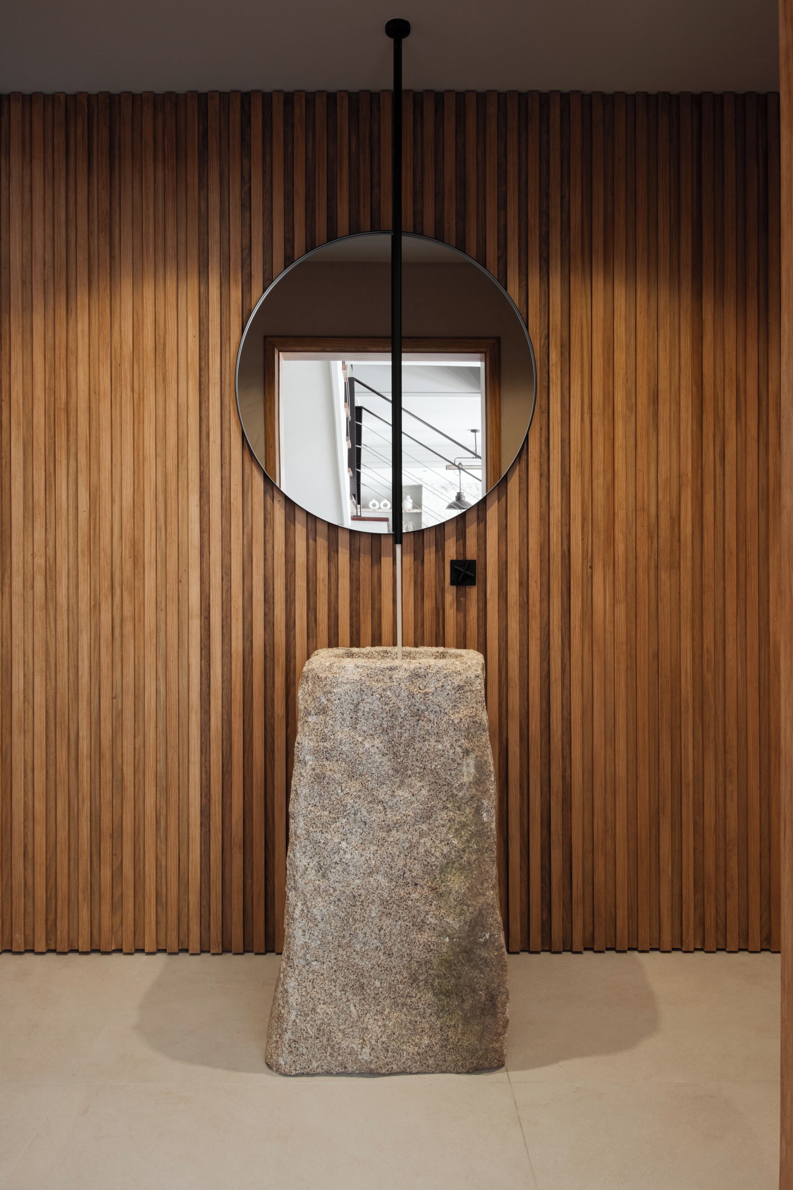 A room with a wooden slat wall, a round mirror, and a granite pedestal.