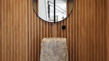 A room with a wooden slat wall, a round mirror, and a granite pedestal.