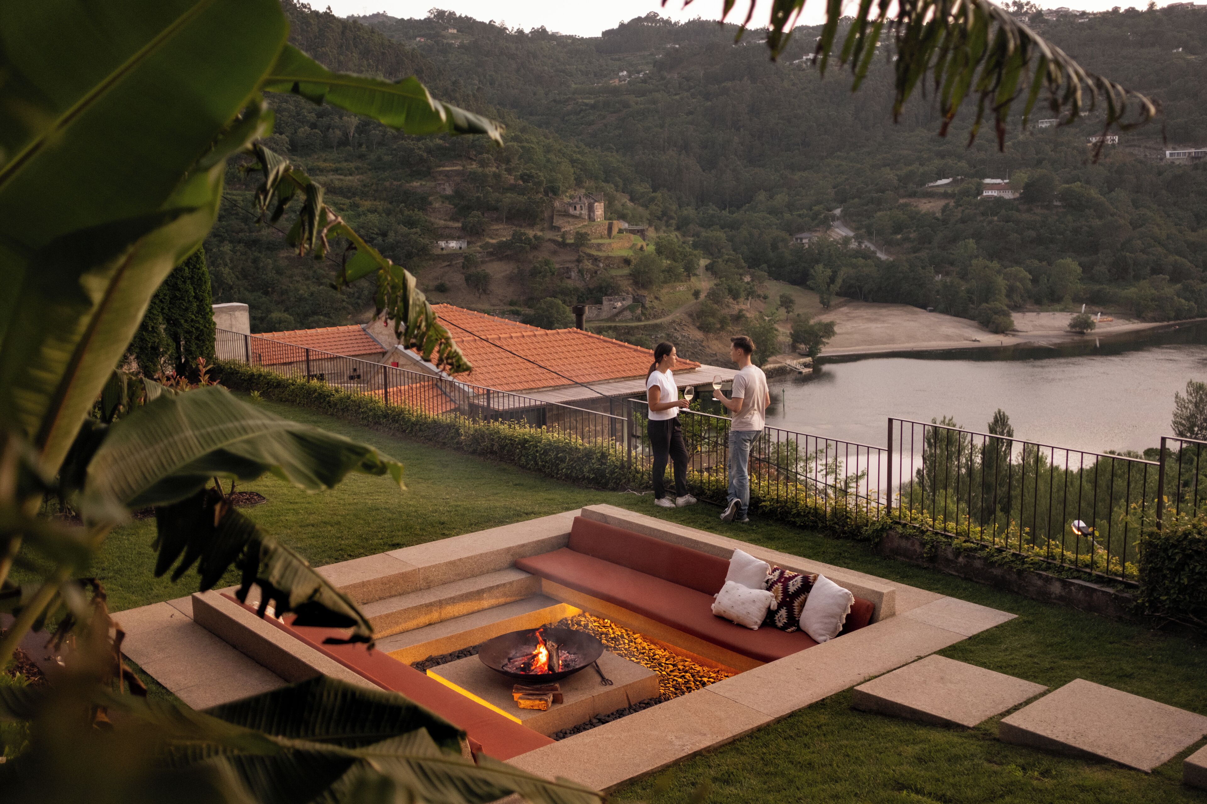 A terrace with a fire pit, seating area, and a view of a lake and hills.