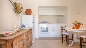 Een kleine keuken met witte kastjes, een fornuis en een spoelbak. Er is een houten kastje met servies en een vaas met bloemen op het aanrecht.