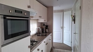 A modern kitchen with stainless steel appliances, a built-in oven, and a gas stove. There is a sink with a faucet, a coffee maker, and a kettle. The kitchen has white cabinets and a wooden countertop. - Pretty chalet with free WiFi on a friendly camping site (Serooskerke)