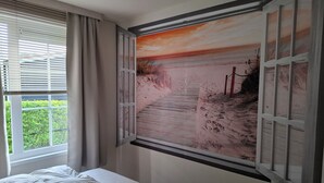 A bedroom with a bed, a window with blinds, and a wall-mounted painting of a beach scene. - Pretty chalet with free WiFi on a friendly camping site (Serooskerke)