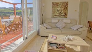 A living room with a beige sofa, a coffee table with books, and a Buddha painting on the wall. - CT 100 - Antes Penthouse (Mijas)
