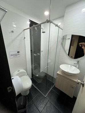 Une salle de bain moderne avec une douche à parois de verre, des toilettes blanches et un lavabo avec un miroir au-dessus.