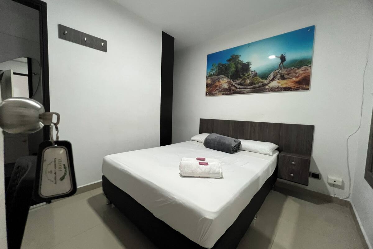Ein Hotelzimmer mit Bett, einem Bild an der Wand, einem Kleiderständer und einem Schlüsselkartenhalter.