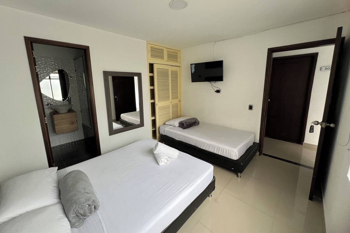 Ein Hotelzimmer mit zwei Betten, einem Fernseher, einem Badezimmer mit Spiegel und einem Kleiderschrank.