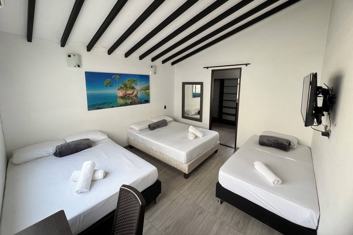 Ein Hotelzimmer mit drei Betten, einem Meeresblick-Gemälde, einem Spiegel und einem Fernseher.