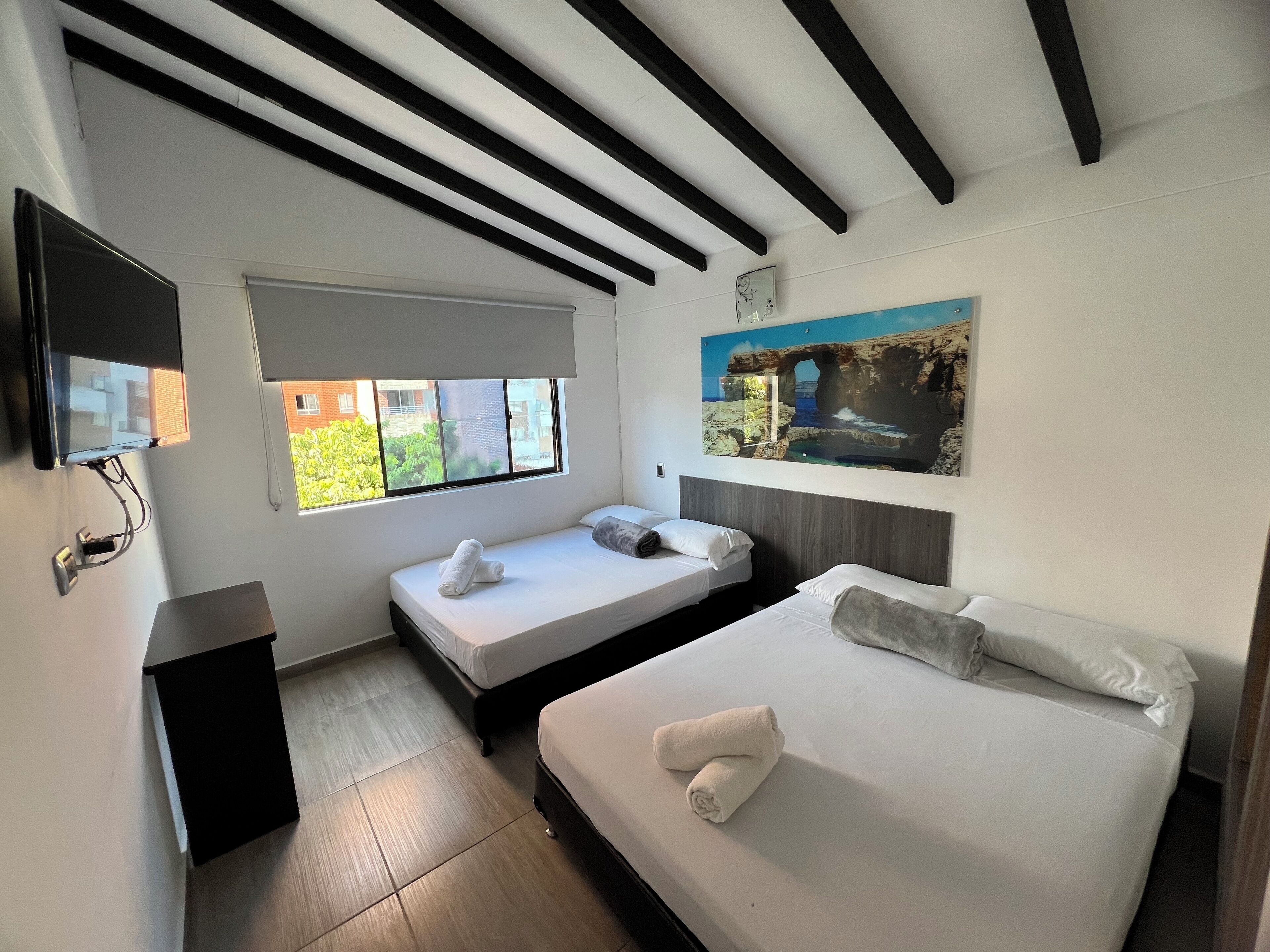 Een hotelkamer met twee bedden, een televisie en een raam met uitzicht op groen en gebouwen.