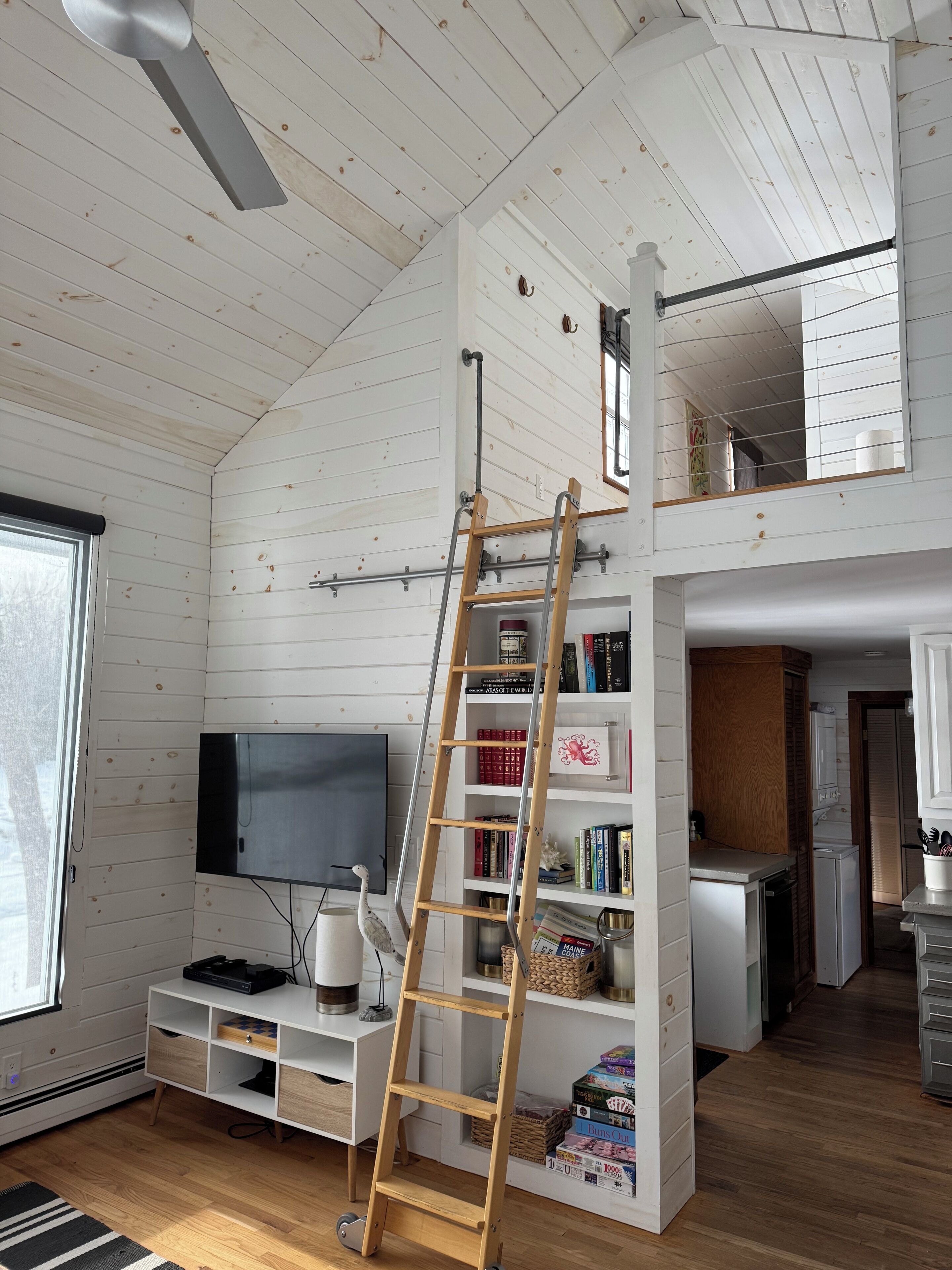 Ein Loft-Zimmer mit Holzleiter, Flachbildfernseher und Bücherregal.