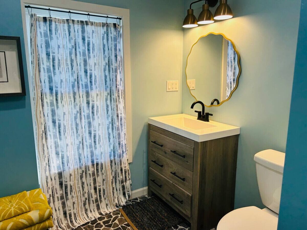 A bathroom with a white sink, wooden vanity, a round mirror, and a toilet.