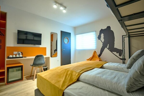A modern hotel room with a bed, a desk with a computer, a TV, and a window with blinds. - Ice Premium Apartments  (Veszprem)