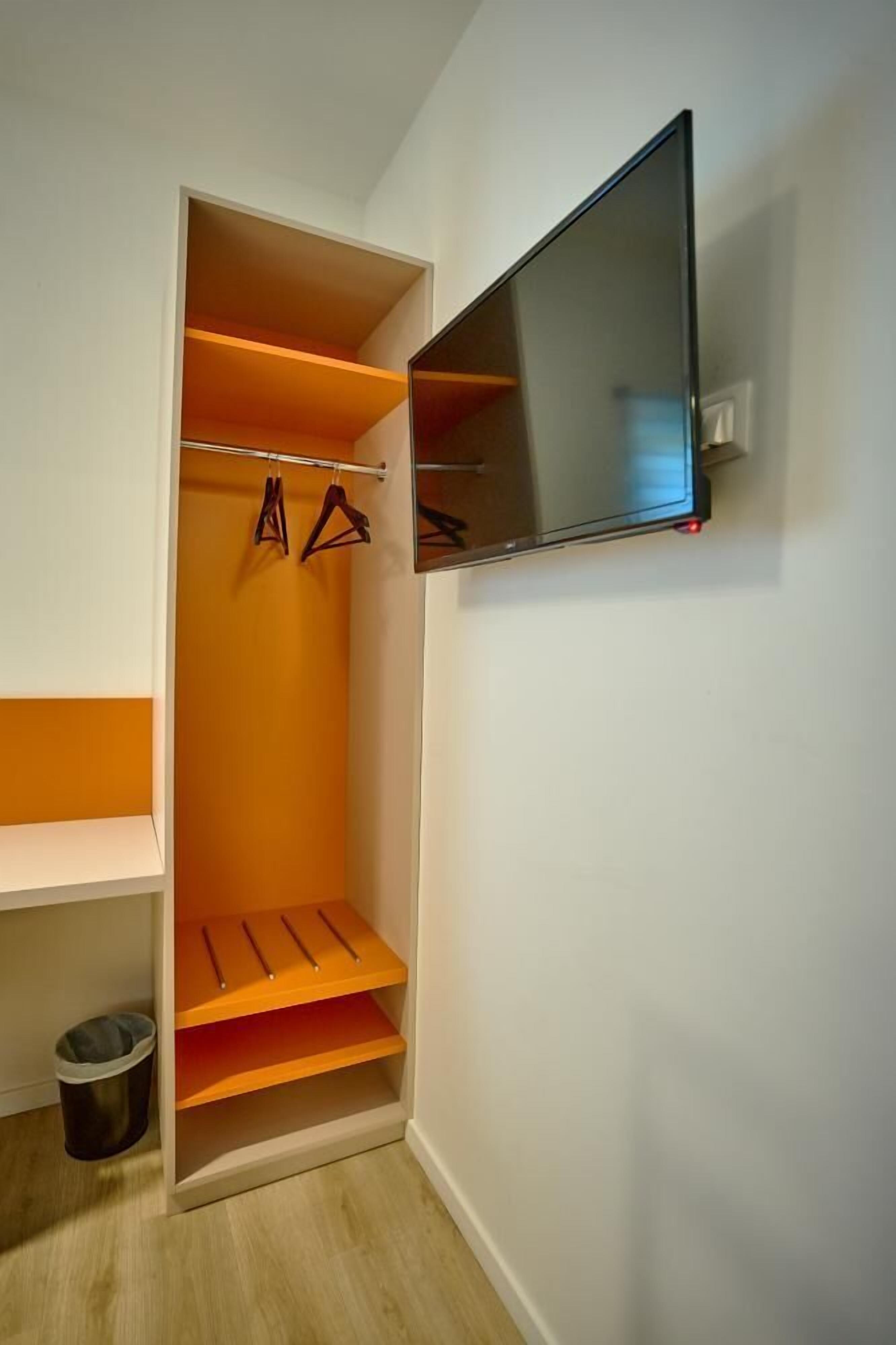 Ein begehbarer Kleiderschrank mit Regalen, einer Kleiderstange, einem Mülleimer und einem an der Wand montierten Fernseher.
