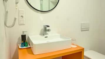 Een moderne badkamer met een witte wastafel, een ronde spiegel, een haardroger en een toilet.