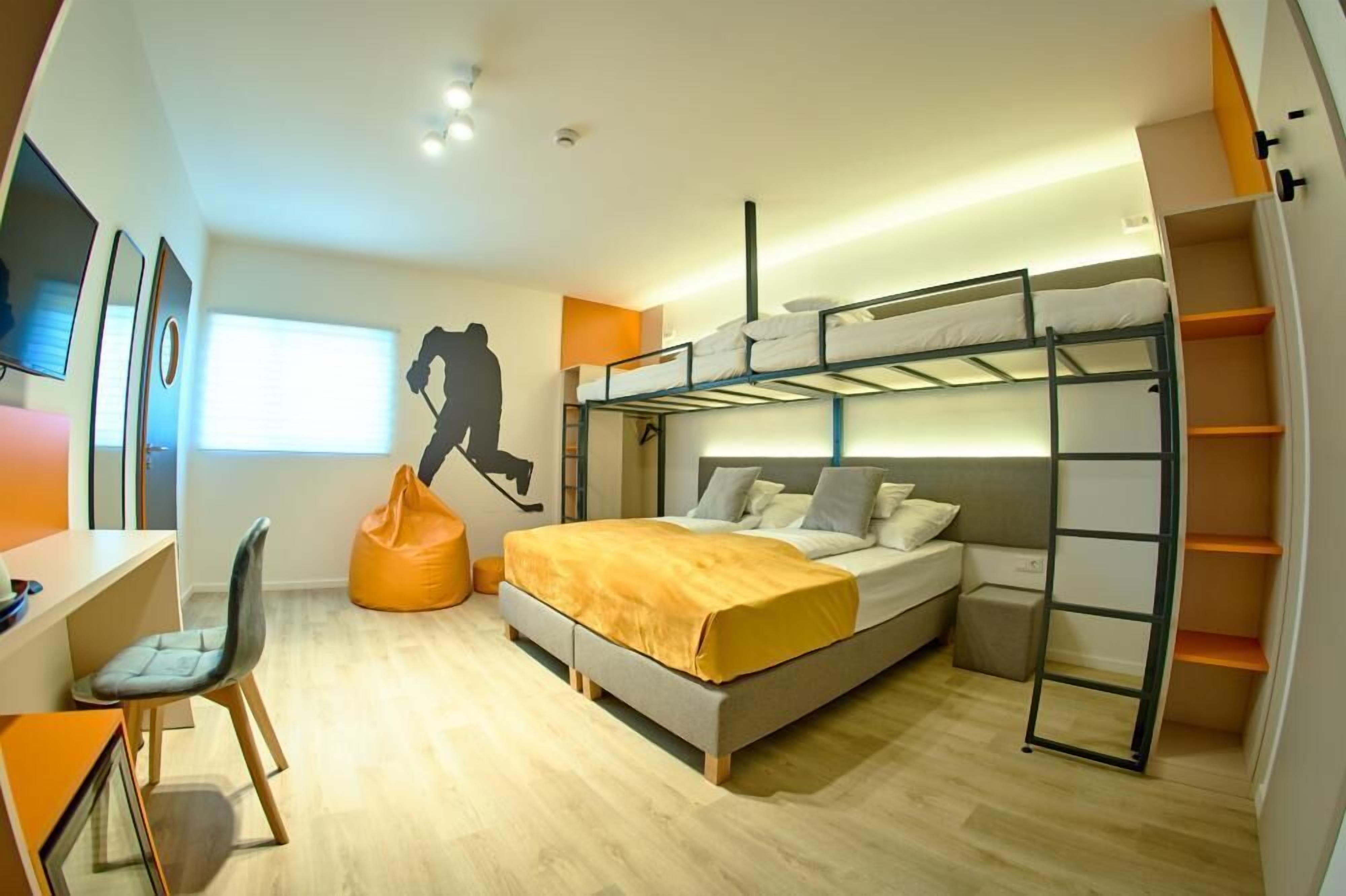 Quarto moderno com beliches, escrivaninha e poltrona de encosto.