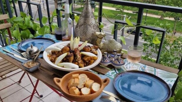 A dining table set with plates, bowls, and utensils on a balcony with a view of the street.