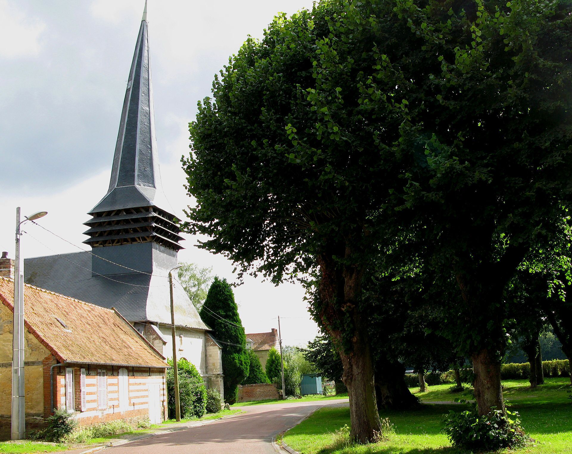 Een kerk met een hoge spits en een grote boom ervoor.
