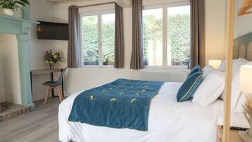 Un dormitorio con cama, escritorio, silla, televisor y ventana con cortinas.
